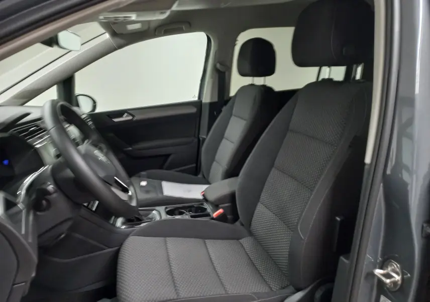 Vue intérieure côté conducteur du Volkswagen Touran 2025 gris Dauphin, montrant les sièges avant et le volant.