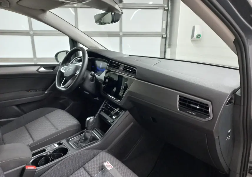 Vue intérieure côté conducteur du Volkswagen Touran 2025 gris dauphin, avec tableau de bord moderne et boîte automatique.