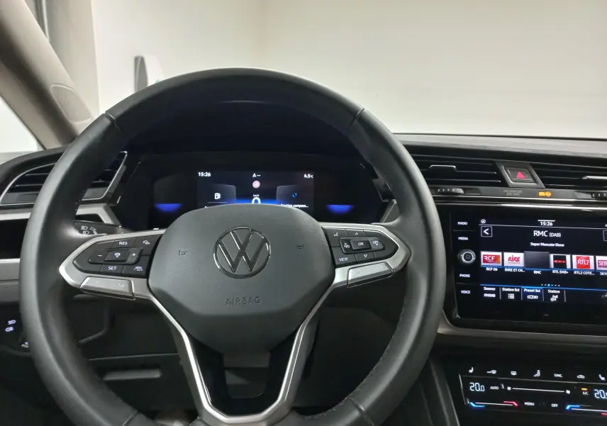 Vue intérieure centrée sur le volant multifonction d’un Volkswagen Touran 2025, tableau de bord et écran tactile visibles.