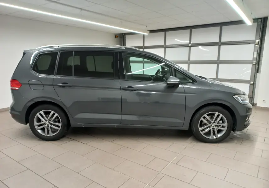 Vue de profil côté gauche du Volkswagen Touran 2025 gris dauphin métallisé avec jantes alliage en intérieur showroom.