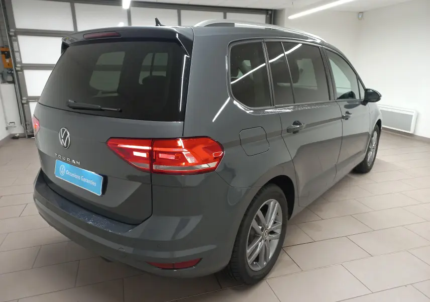Vue 3/4 arrière droite d'un Volkswagen Touran 2025 gris dauphin métallisé, avec vitres teintées et jantes alliage.