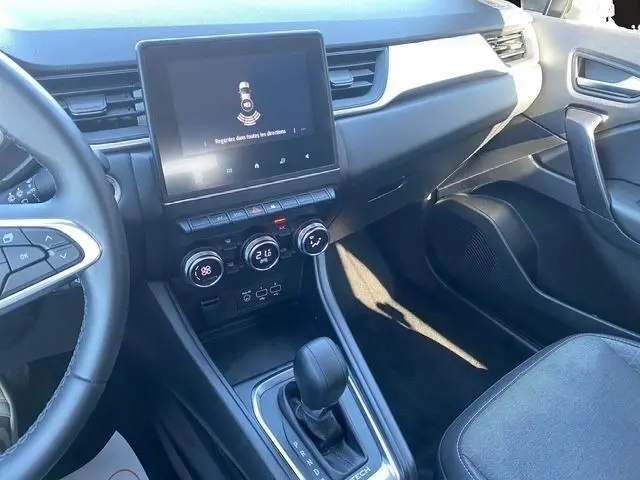 Vue intérieure du tableau de bord et console centrale du Renault Captur gris clair, avec écran tactile et levier de boîte automatique.