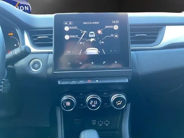 Tableau de bord central du Renault Captur gris clair 2023 avec écran tactile et commandes climatisation visibles de face.