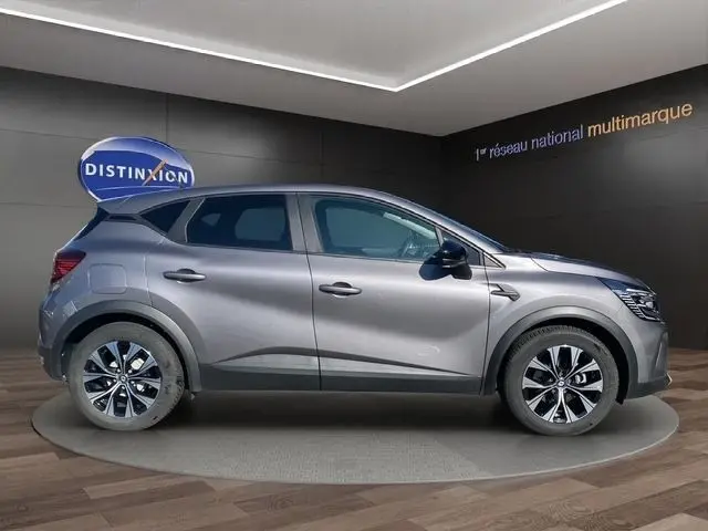 Profil droit du Renault Captur gris clair 2023, version E-Tech full hybrid 145, sur plateforme en showroom.