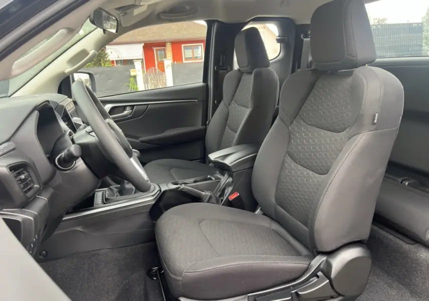 Vue intérieure côté conducteur de l'Isuzu D-MAX 2026 avec sièges tissu gris et accoudoir central avant.