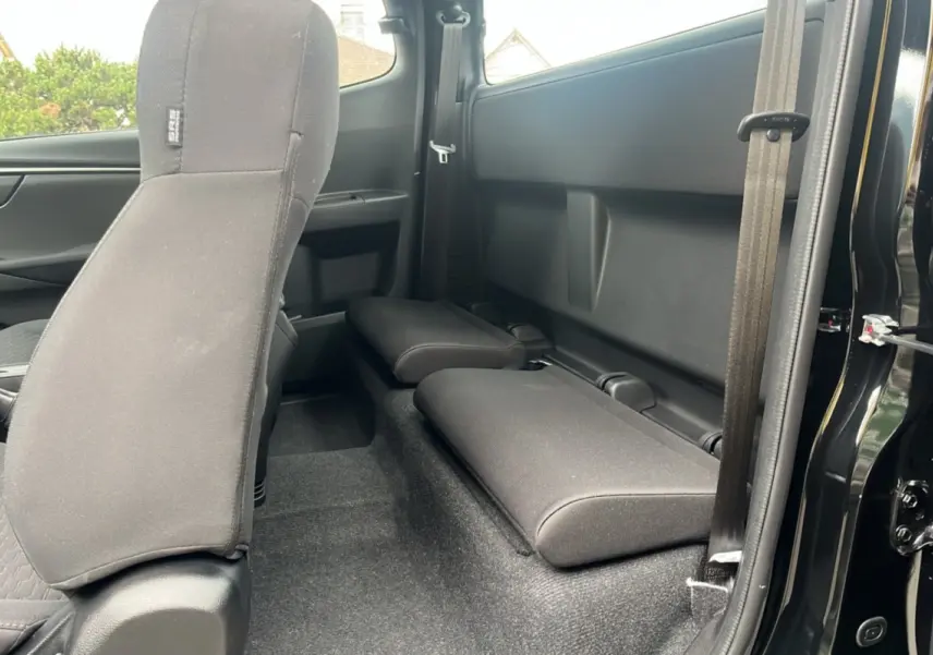 Vue intérieure côté droit du pick-up Isuzu D-MAX 2026 noir, montrant les strapontins arrière rabattus et la sellerie tissu noire.