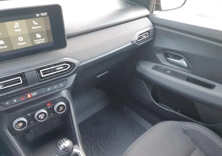 Intérieur de la Dacia Sandero 2024 côté passager, tableau de bord gris avec écran tactile et climatisation automatique.