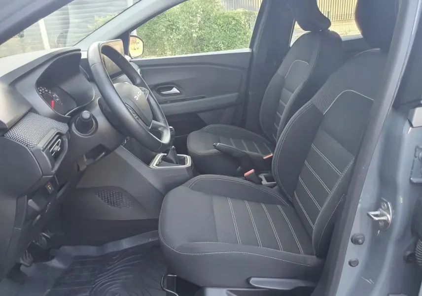 Vue intérieure côté conducteur de la Dacia Sandero gris urbain 2024 avec sièges avant chauffants et volant réglable.