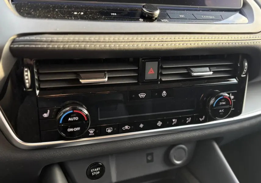 Vue rapprochée de la console centrale du Nissan Qashqai noir, montrant les commandes de climatisation automatique bi-zone et bouton Start/Stop.