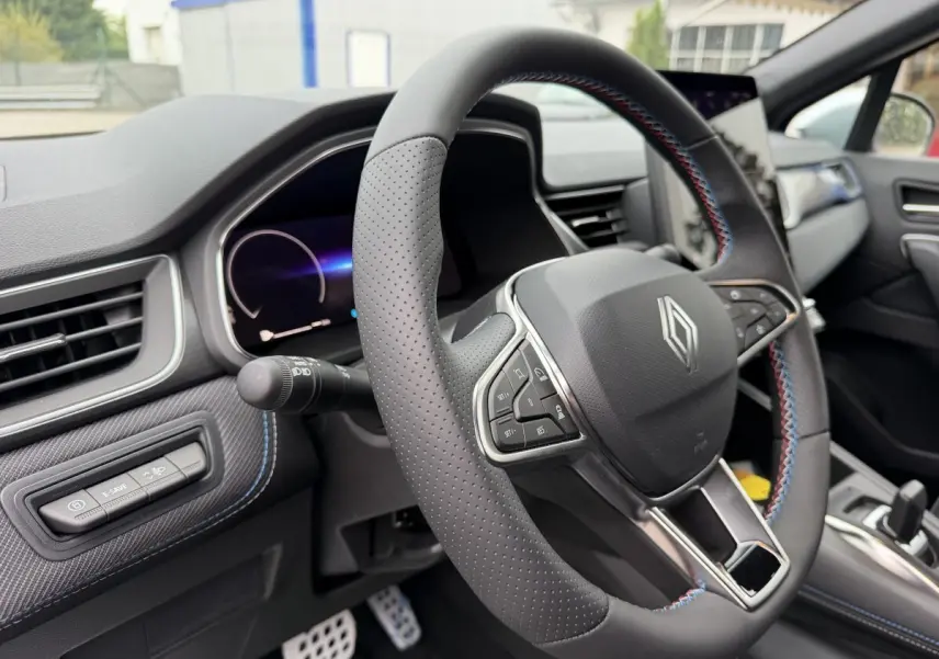 Vue intérieure centrée sur le volant cuir perforé avec surpiqûres bleues et tableau de bord numérique du Renault Captur bleu esprit Alpine.