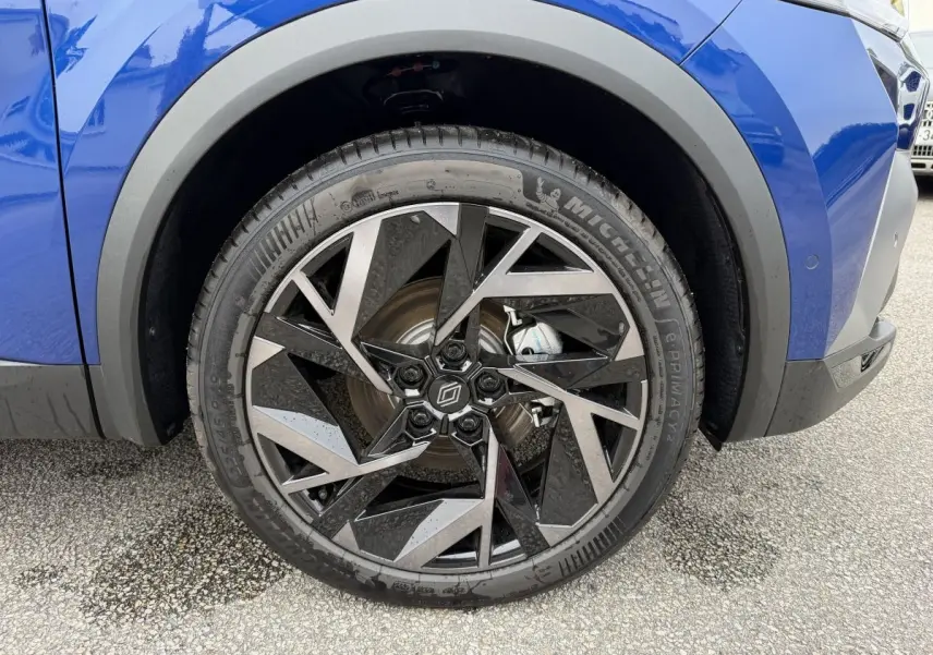 Gros plan sur la roue avant droite du Renault Captur bleu esprit Alpine, jante alliage au design géométrique noir et argent.