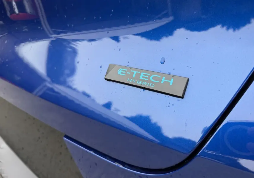 Gros plan sur l'emblème E-TECH Hybrid bleu clair sur la carrosserie bleue brillante d'une Renault Captur.