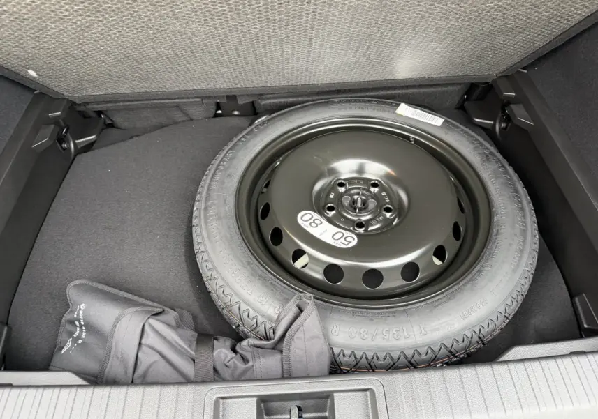 Vue plongeante sur la roue de secours noire et l’espace de rangement dans le coffre du Renault Captur bleu esprit Alpine.