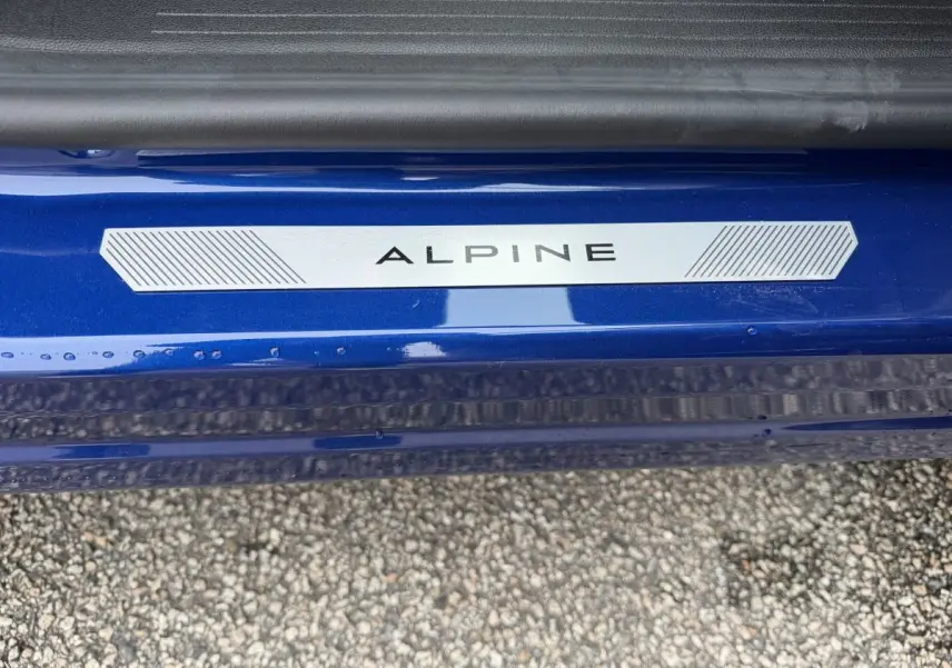 Gros plan sur la plaque Alpine sur le seuil de porte bleu d'un Renault Captur esprit Alpine full hybrid.