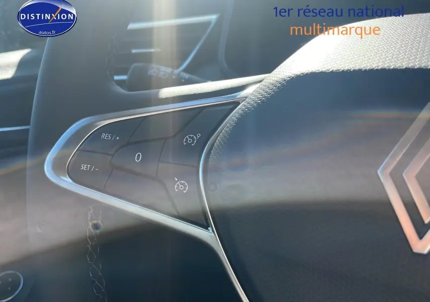 Gros plan sur les commandes du volant multifonction de la Renault Clio V, avec éclairage naturel et logo visible.