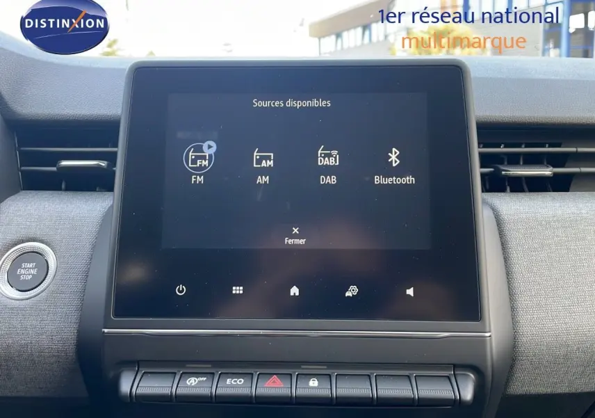 Écran tactile central de la Renault Clio 1.5 DCI 100ch Evolution 2025 avec commandes radio et bouton start/stop visible.