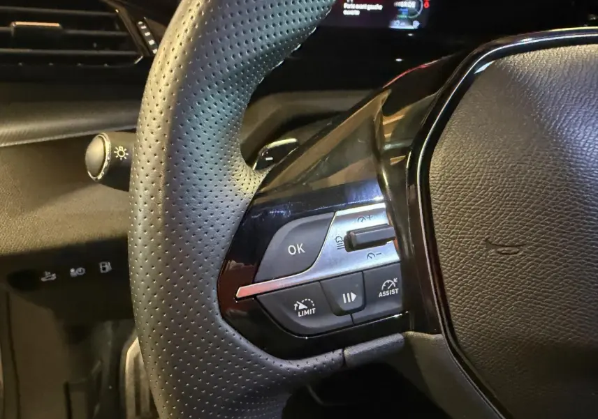 Gros plan sur le volant perforé noir avec commandes multifonctions et tableau de bord numérique partiel de la Peugeot 408 gris Selenium.