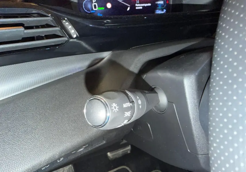 Gros plan sur la commande des feux à gauche du volant perforé dans l’habitacle sombre du Peugeot 408 gris.