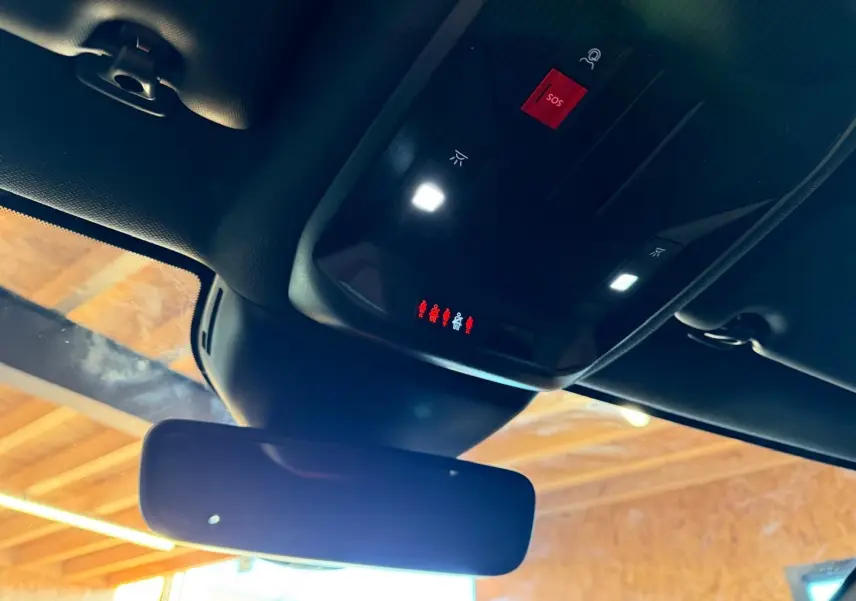 Vue intérieure du plafond noir Mistral avec rétroviseur et commandes d'éclairage et bouton SOS rouge du Peugeot 408 gris hybride rechargeable.