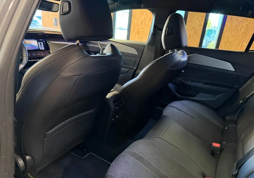Vue intérieure arrière droite de la Peugeot 408 2025, sièges noirs tri-matières avec surpiqûres vertes et détails aluminium.