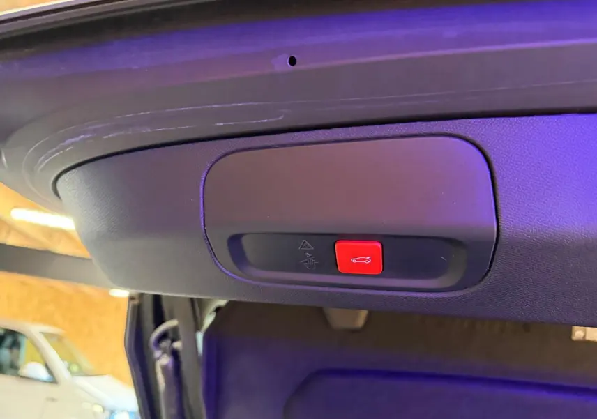 Gros plan sur le bouton rouge d'ouverture motorisée du hayon d'une Peugeot 408 gris Selenium, intérieur coffre visible.