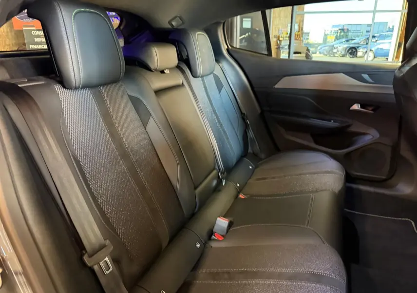 Vue intérieure des sièges arrière noirs avec surpiqûres vertes et panneaux de porte gris sur Peugeot 408 2025.