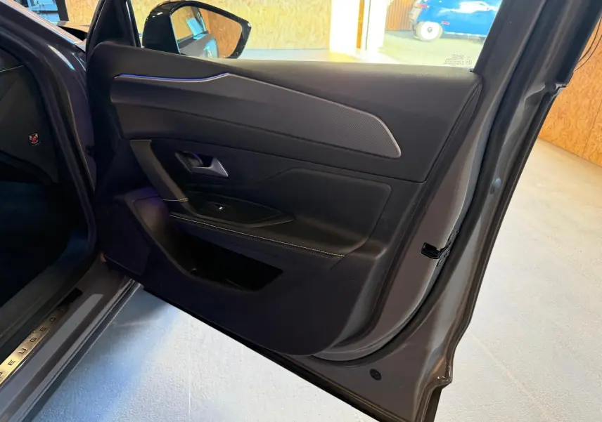 Vue intérieure côté gauche de la porte arrière grise du Peugeot 408 2025 avec surpiqûres vertes et éclairage d'ambiance bleu.