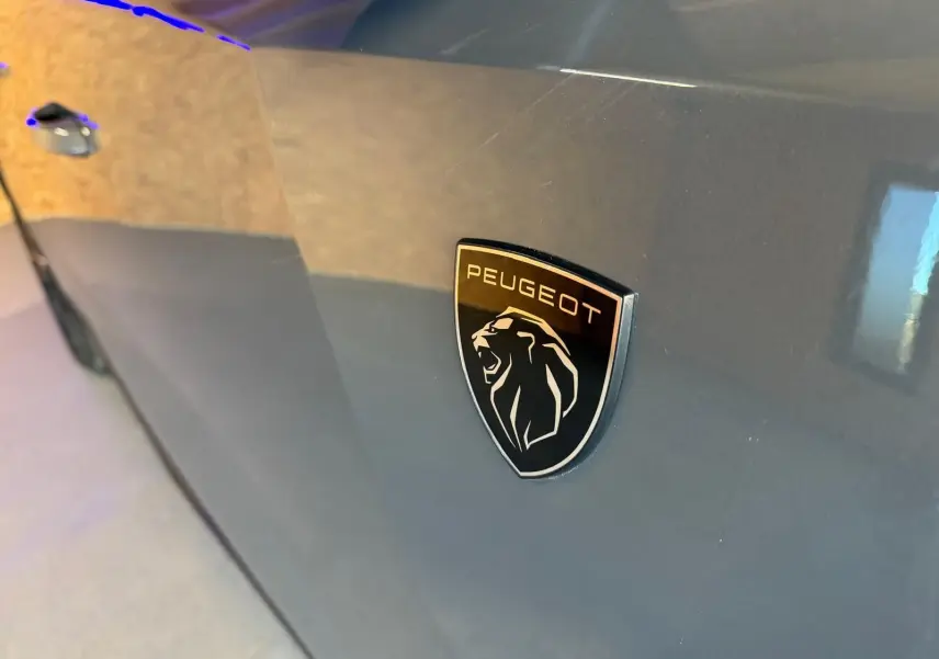 Gros plan sur l’écusson Peugeot noir brillant sur la porte côté gauche d’une 408 gris métallisé.