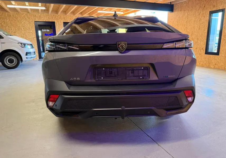 Vue arrière d'une Peugeot 408 gris Selenium avec feux arrière à effet griffe et badge Hybrid visible en intérieur.