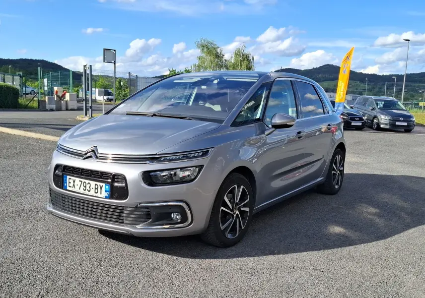 Citroën C4 Picasso gris clair vue 3/4 avant droit, avec jantes alliage noires et toit panoramique visible.