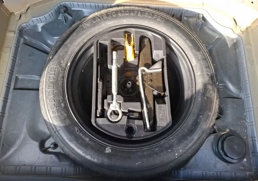 Vue plongeante sur la roue de secours et le kit d'outils dans le coffre d'une Citroën C4 Picasso gris clair 2018.