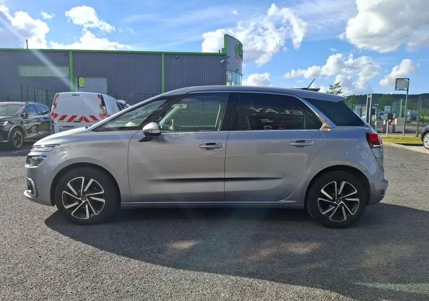 Vue de profil côté gauche d'une Citroën C4 Picasso gris clair avec jantes alliage 17 pouces sur parking extérieur.