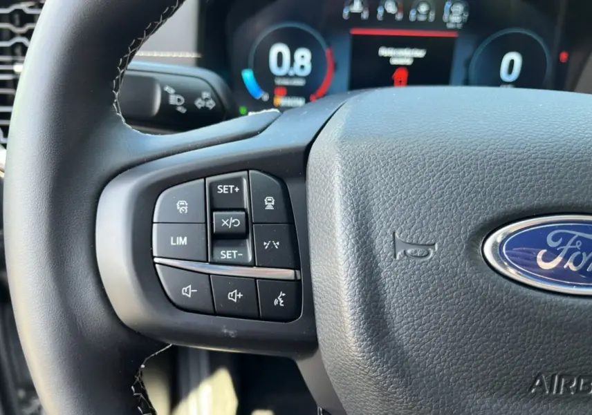 Gros plan sur le volant multifonctions en cuir du Ford Ranger gris, avec commandes de régulateur et logo Ford visible.