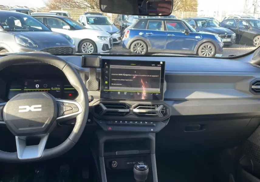 Vue intérieure avant du tableau de bord noir du Dacia Duster 2026 avec écran tactile et volant multifonction.