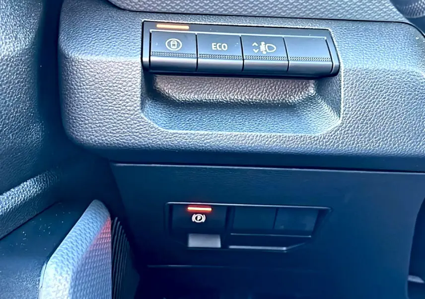 Vue rapprochée du tableau de bord noir du Dacia Duster 2026, avec boutons de commande Eco et frein à main électronique.