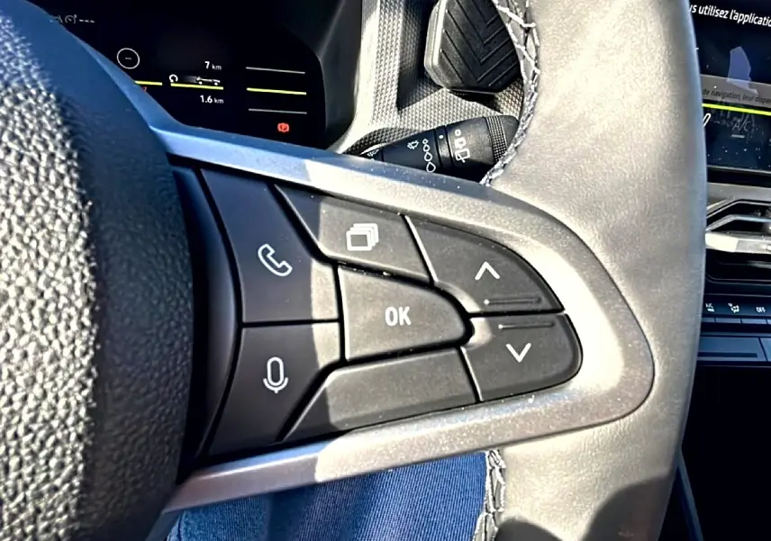 Gros plan sur les commandes multifonctions du volant noir du Dacia Duster 2026, avec écran tactile en arrière-plan.