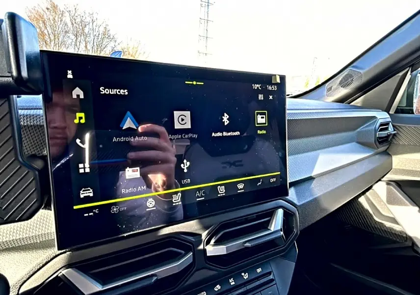 Vue intérieure du tableau de bord du Dacia Duster 2026, écran tactile multifonction et aérateurs hexagonaux noirs.