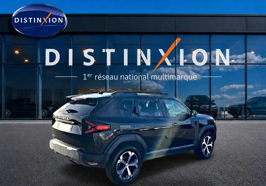 Vue 3/4 arrière droite d'un Dacia Duster noir 2026 avec jantes alu, barres de toit et becquet arrière visible.