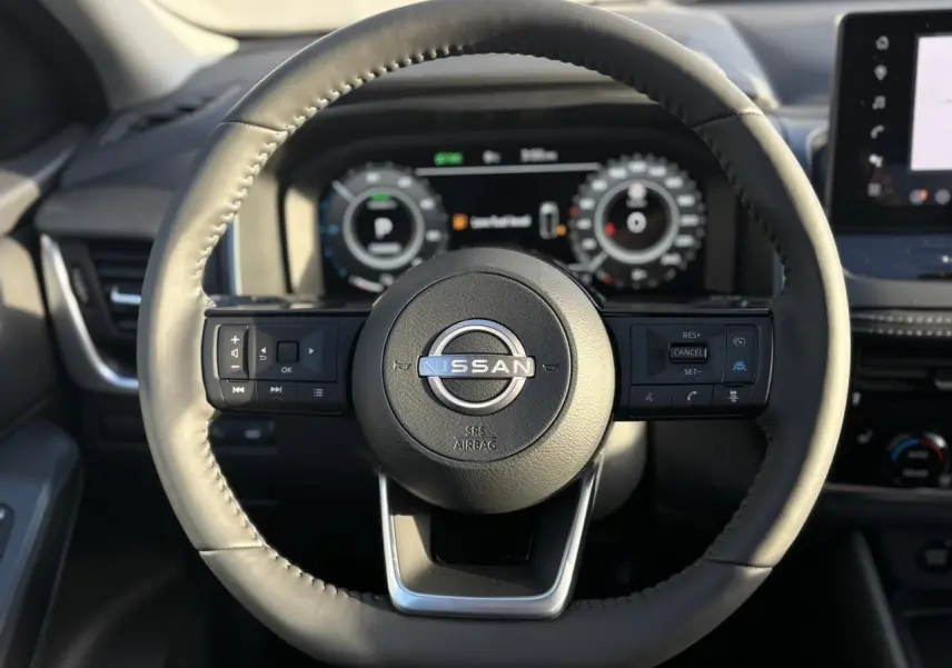 Vue rapprochée du volant noir du Nissan Qashqai 2026 avec commandes intégrées et tableau de bord numérique en arrière-plan.