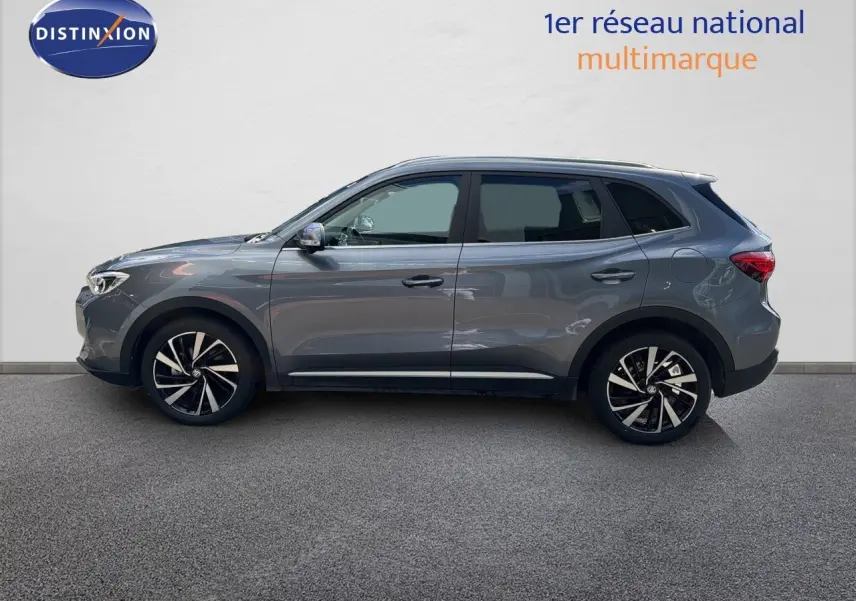 Vue de profil côté gauche du MG MOTOR ZS 1.5L HYBRID+ 197CH LUXURY 2025 en gris Hampstead avec jantes alliage bicolores.