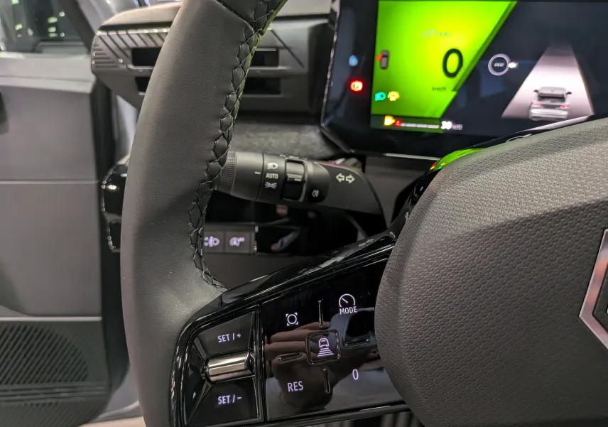 Gros plan sur le volant noir de la Renault Clio VI avec commandes intégrées et tableau de bord numérique vert vif.