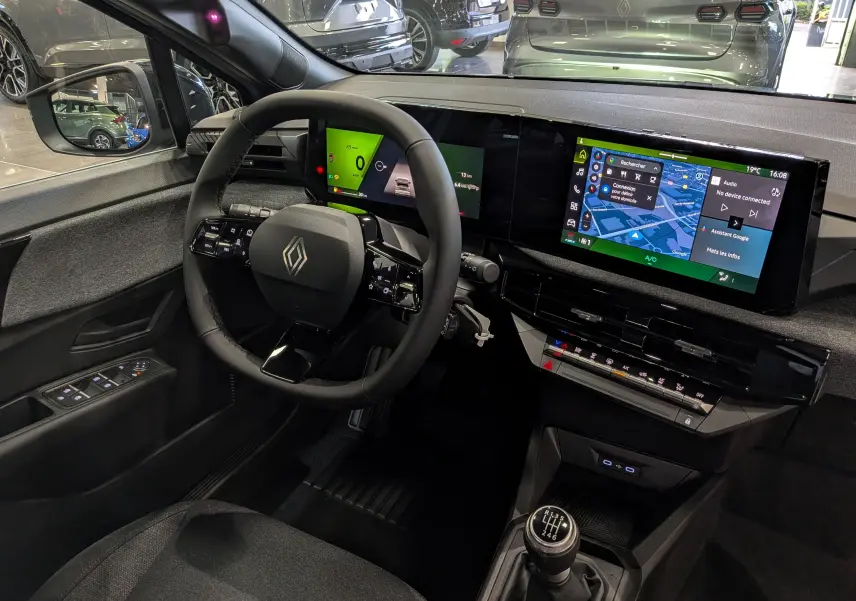 Vue intérieure côté conducteur de la Renault Clio VI gris Rafale, avec tableau de bord numérique et boîte manuelle.