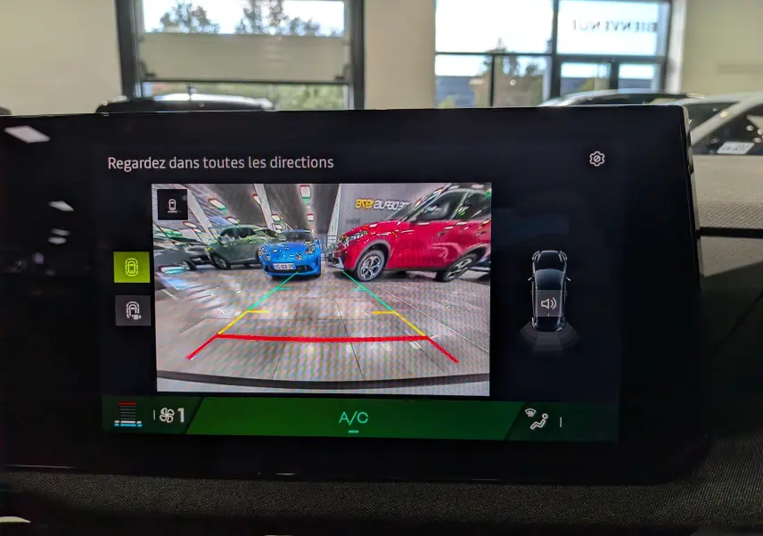 Écran intérieur de la Renault Clio VI gris Rafale montrant la caméra de recul avec vue sur voitures en parking.