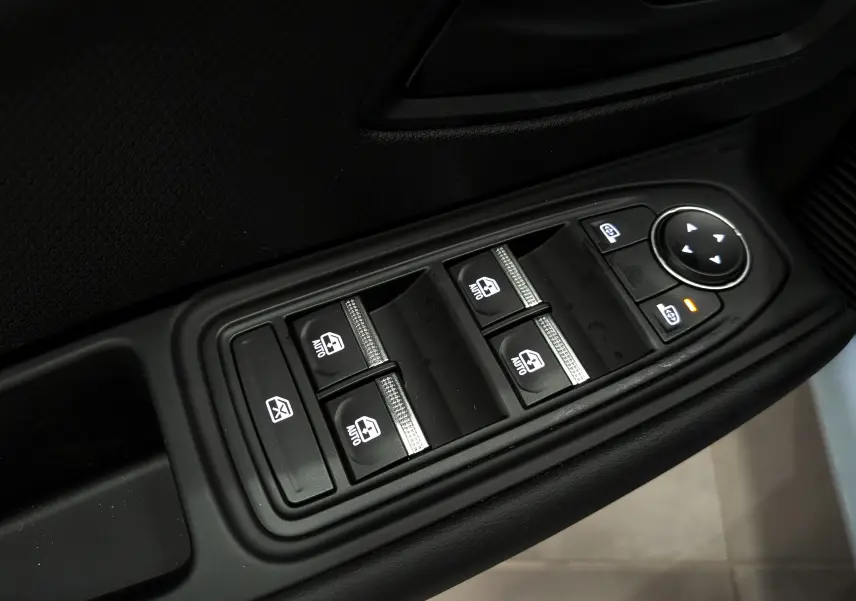 Gros plan sur les commandes des vitres électriques et rétroviseurs sur la porte côté gauche d’une Renault Clio VI Gris Rafale.