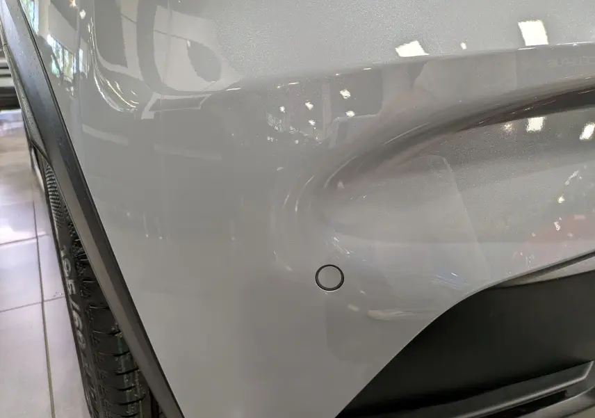 Gros plan sur l'aile avant droite gris Rafale de la Renault Clio VI avec capteur de stationnement visible.