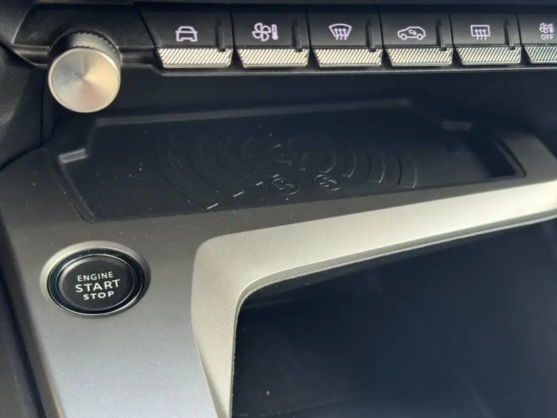 Détail intérieur du tableau de bord de la Peugeot 308 2024, bouton start/stop et rangée de commandes au-dessus d’un espace de recharge sans fil.