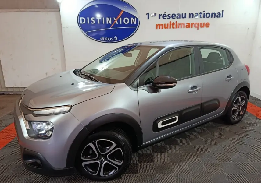 Vue 3/4 avant droite d'une Citroën C3 2024 gris clair avec protections latérales noires et jantes noires à inserts argentés.