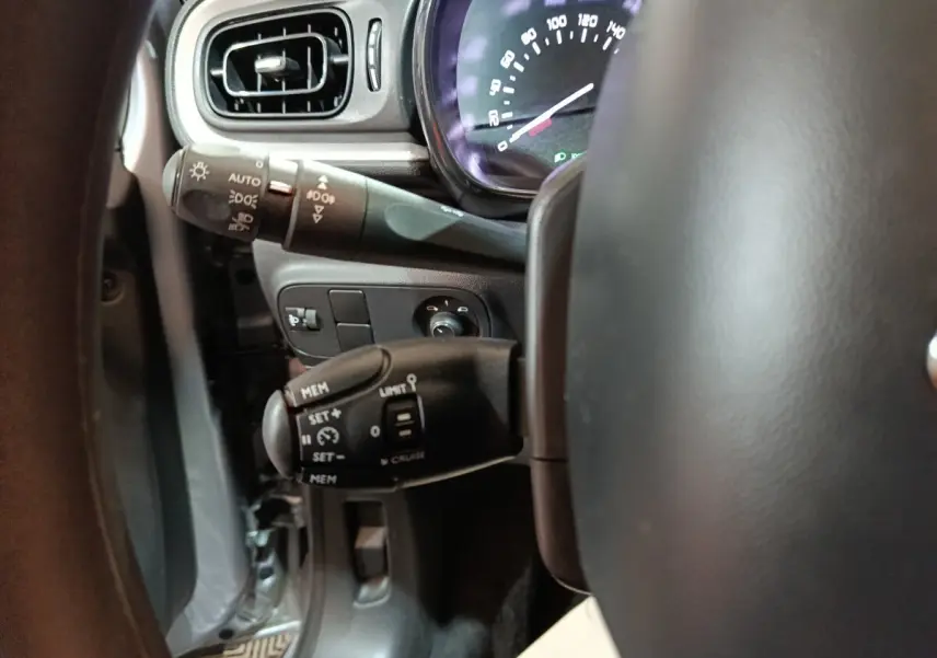 Gros plan sur la partie gauche du volant d'une Citroën C3 gris clair 2024, montrant commandes de régulateur et tableau de bord.