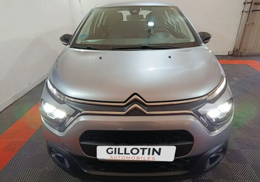 Vue avant d'une Citroën C3 2024 gris clair avec phares LED allumés dans un garage.