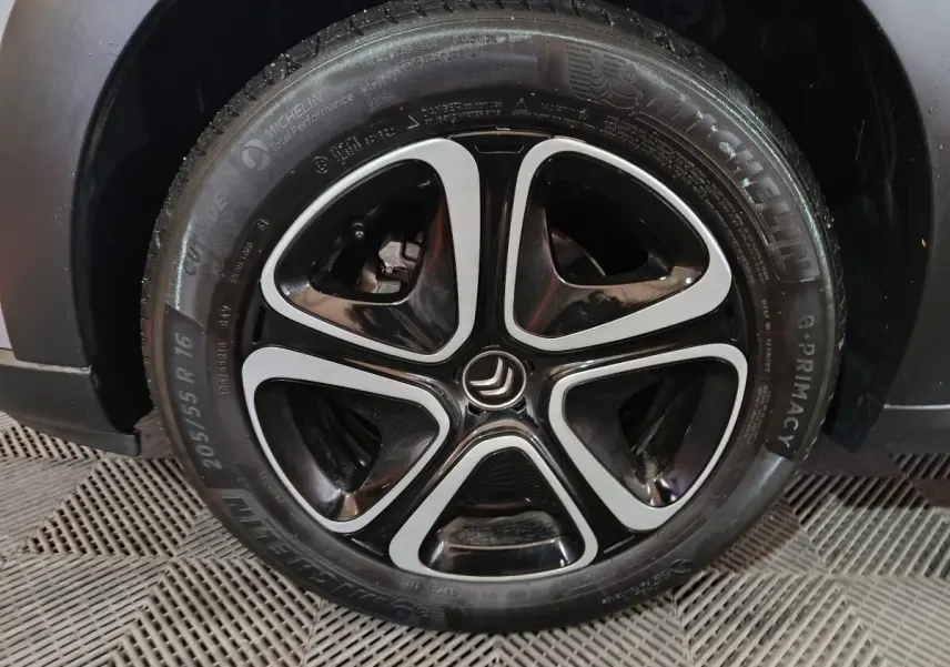 Gros plan sur la roue avant droite d'une Citroën C3 gris clair avec jante alliage noire et argentée au design moderne.